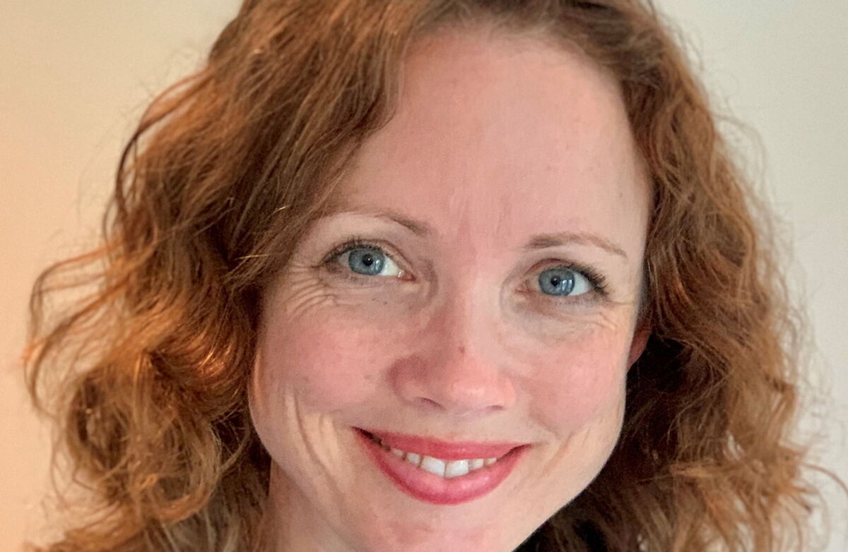 Kvinne med blå øyne og langt rødt hår, smiler