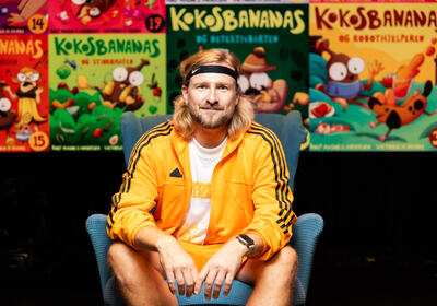Forfatter Rolf Magne G Andersen sitter foran en vegg med bøkene om Kokos Bananas