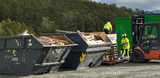 Bilde fra gjenbruksstasjonen langs E10. Bilde av konteinere fylt med materialer. To mennesker som arbeider i bakgrunnen