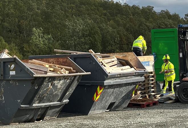 Bilde fra gjenbruksstasjonen langs E10. Bilde av konteinere fylt med materialer. To mennesker som arbeider i bakgrunnen