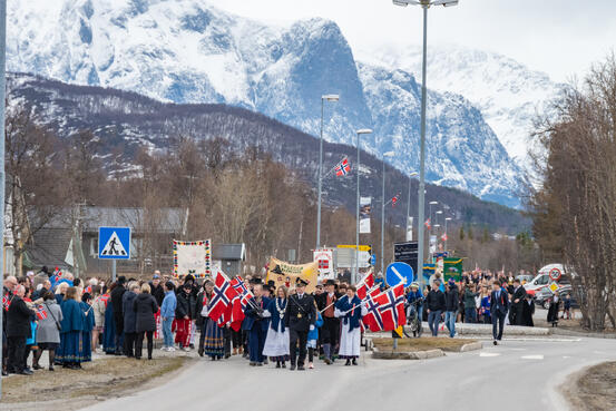 Bildet viser et 17. mai tog med politiet i front, tetter etterfulgt av ordfører og resten av toget. Det er mange glade folk.