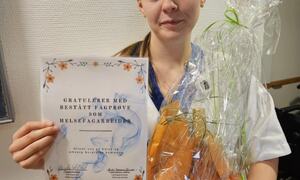 Bildet viser en fornøyd dame som har bestått fagprøven som helsefagarbeider. Hun smiler mens hun holder et diplom og en gave.