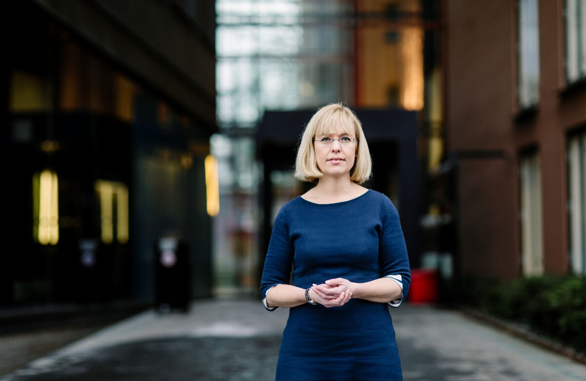 Kvinne med lyst hår, pannelugg og blå øyne smiler mot kameraet. Hun har en blå topp. Bakgrunnen er mørk og utydelig.