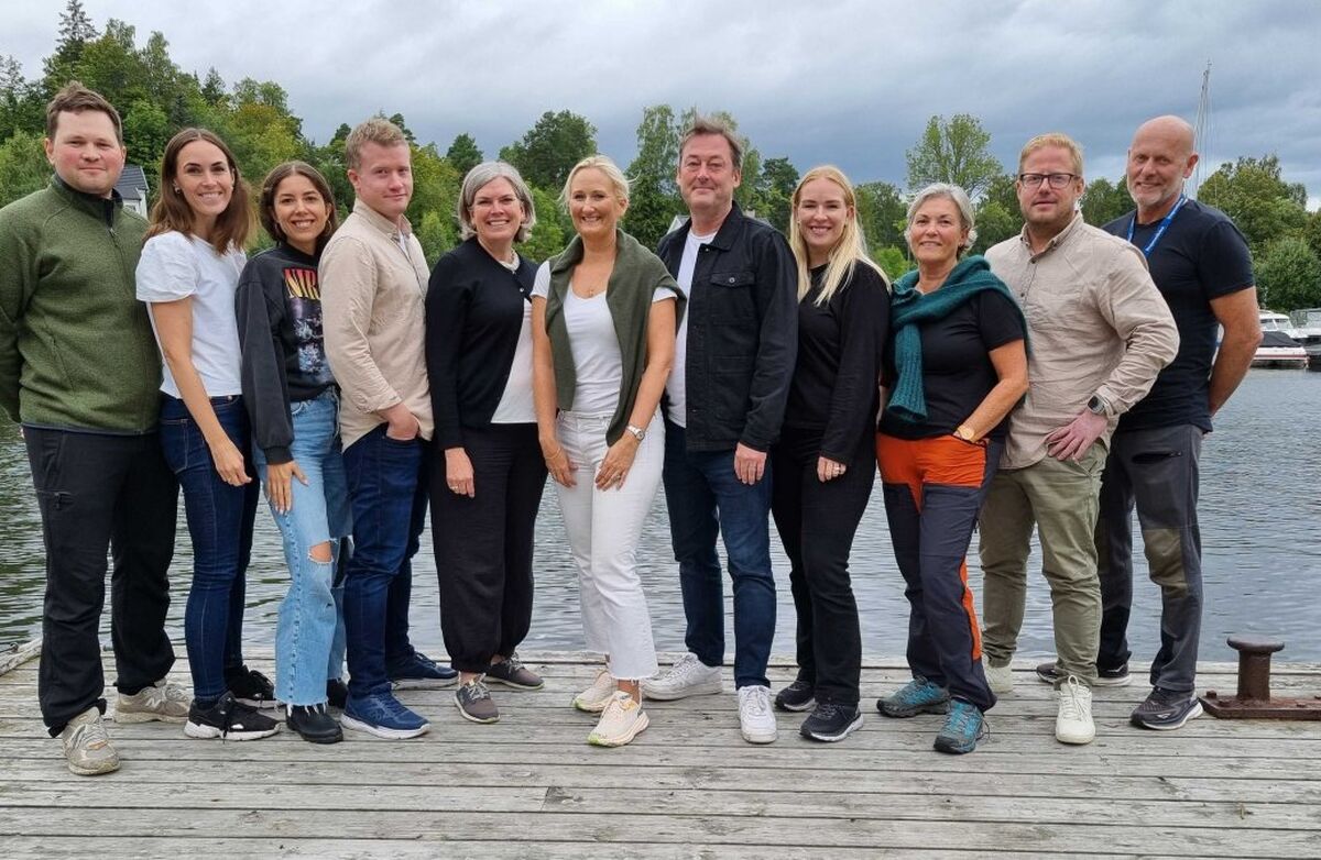 Styret og dei ansatte i Prosperastiftelsen står på en bryggekant med sjø og natur i bakgrunnen.