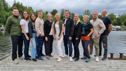 Styret og dei ansatte i Prosperastiftelsen står på en bryggekant med sjø og natur i bakgrunnen.