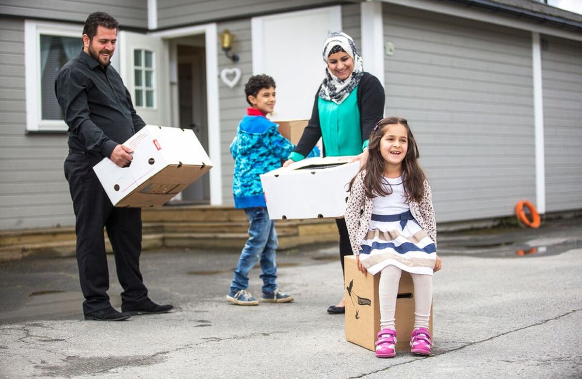 Innvandrerfamilie, to barn og foreldrene utenfor et hus. De har flytteesker, og flytter sannsynligvis inn.