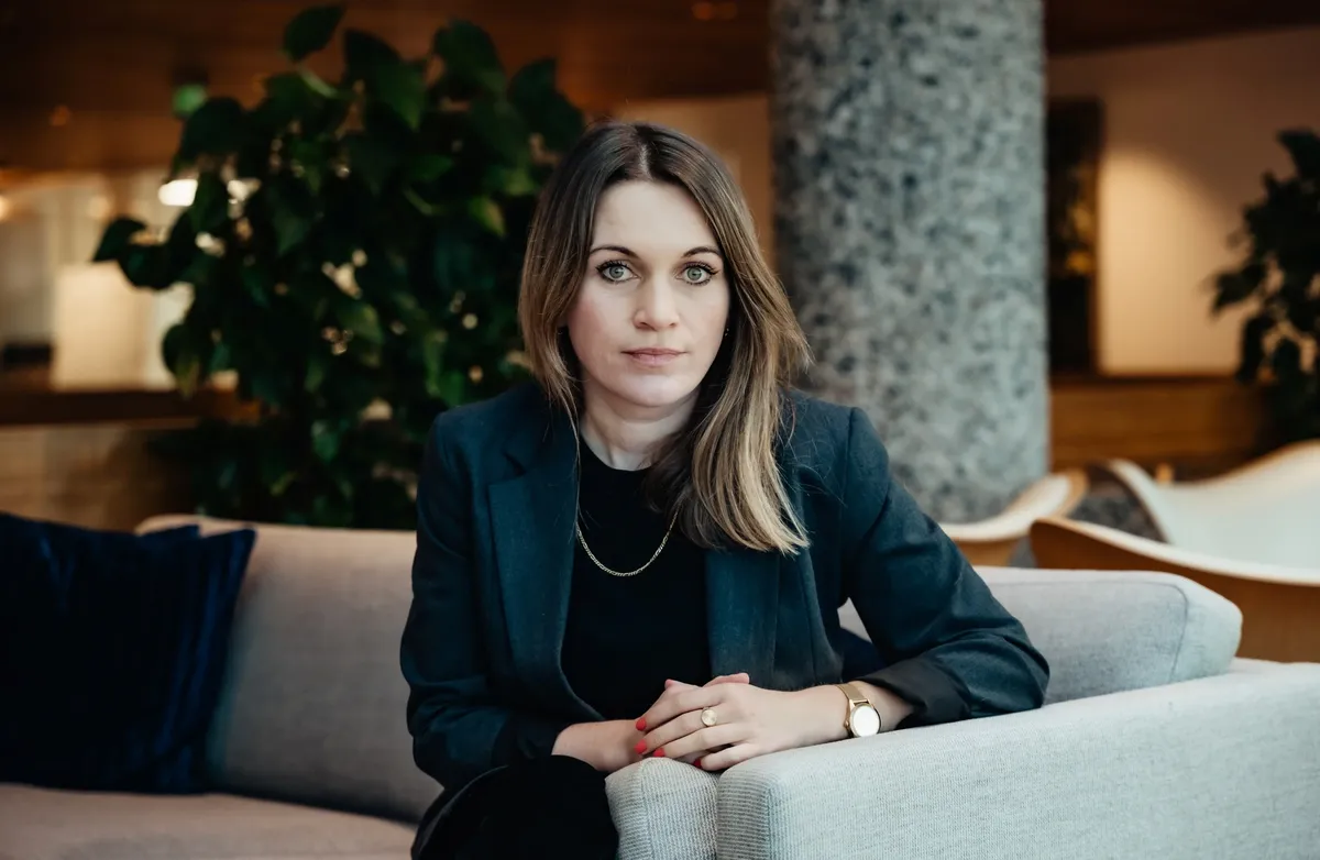 Ingvild von Krogh sitter i en sofa. Brunt hår, brune øyne, mørk jakke, sort bluse, synlig smalt gullkjede, røde negler.