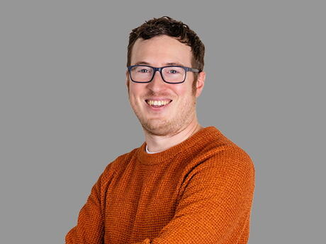 Ung mann med oransje genser, smiler, armene i kors