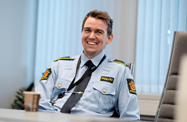 Frode Hauge. Frode Hauge i uniform bak skrivebord og PC. Han smiler bredt.