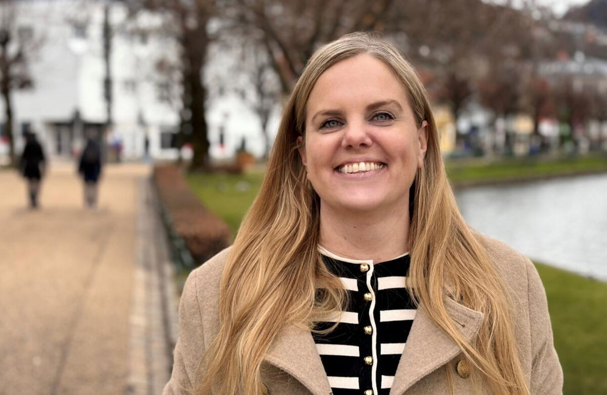 Kvinne utendørs med langt lyst hår og blå øyne, beige jakke.