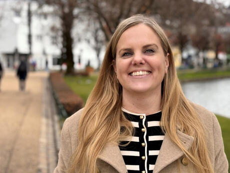 Kvinne utendørs med langt lyst hår og blå øyne, beige jakke.