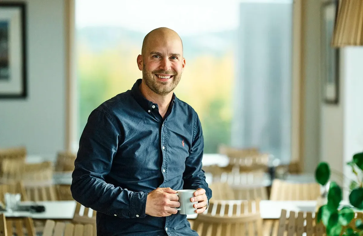 Mann uten hår, smiler, med olaskjorte og kaffekopp