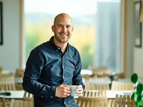 Mann uten hår, smiler, med olaskjorte og kaffekopp