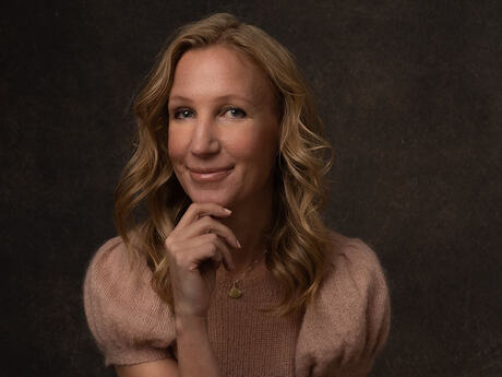 Kvinne med langt lyst hår, en hånd under haken, ser tenksomt mot kamera