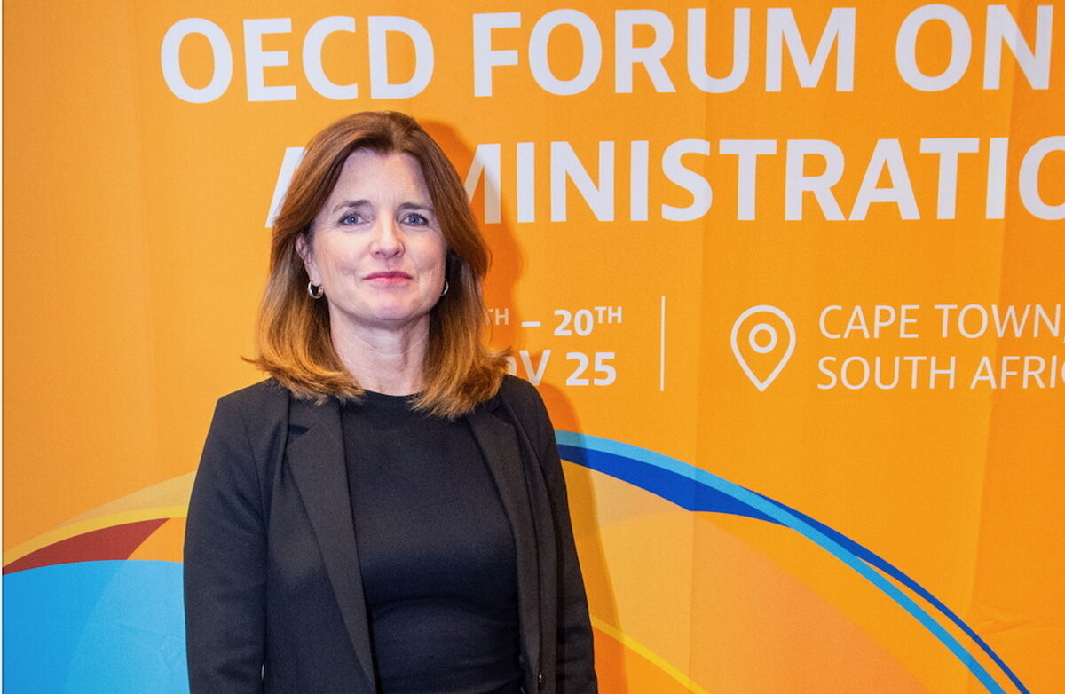 Kvinne med brunt hår står foran et oransje banner med tekst om OECD