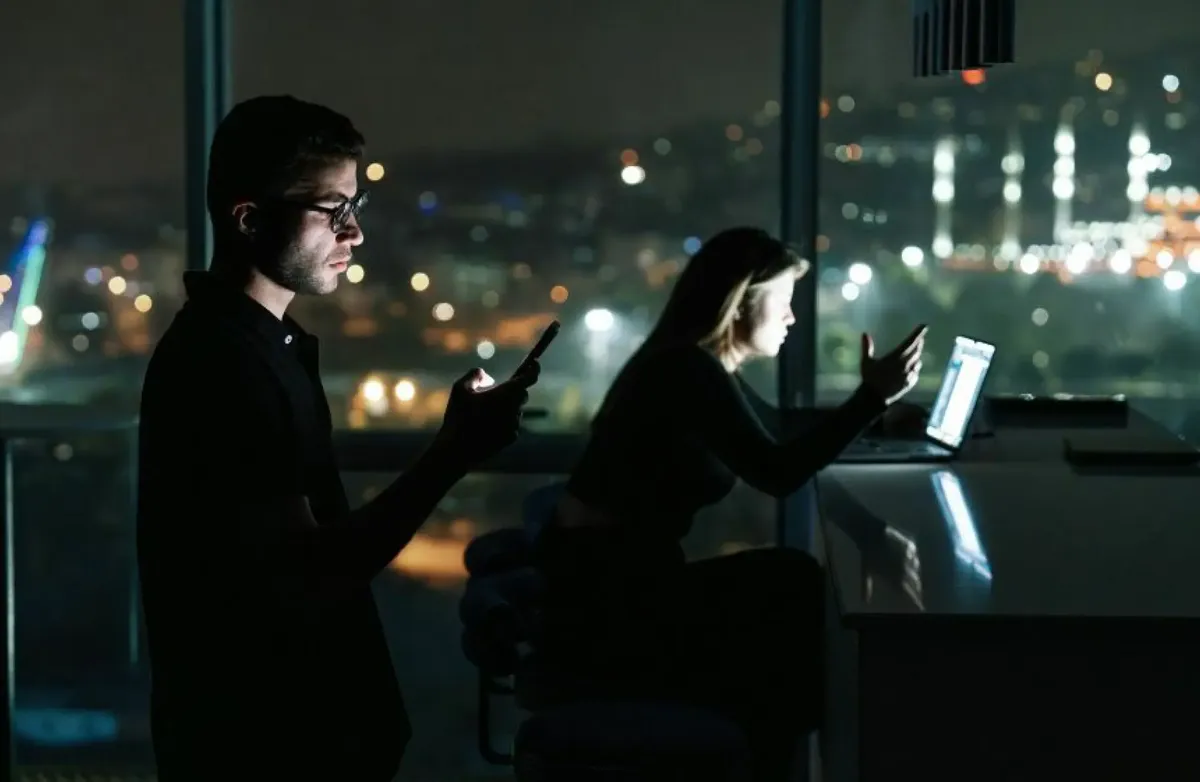 Studier viser at selv om vi liker å si vi er kritiske, så følger vi rådene til KI. Foto: Kurt Ahmet / Unsplash Kvinne og mann i mørkt rom jobber ved skjermer