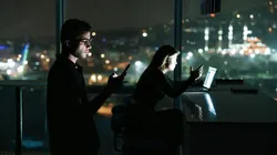 Kvinne og mann i mørkt rom jobber ved skjermer