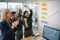 To kvinner og to menn uttrykker arbeidsglede foran en tavle med grafer og ord som tillit og kultur. De har forskjellig etnisitet.