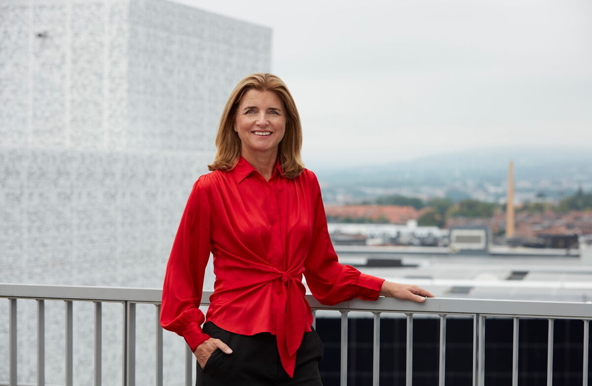 Nina Schanke Funnemark står utendørs, muligens på et tak der hun holder i et rekkeverk med en hånd. Hun smiler, og har på en rød løsthengende bluse. Håret er mellomblondt og langt. I bakgrunnen er det et bymiljø.