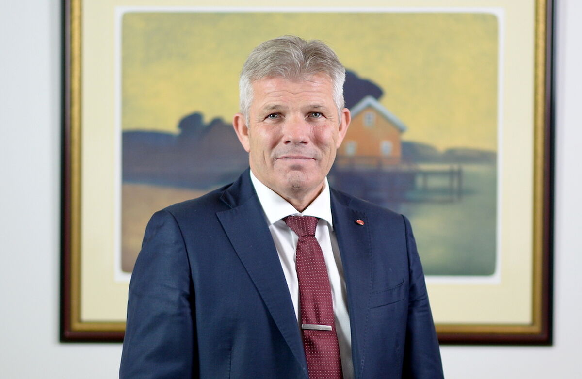 Bjørnar Skjæran med et maleri i bakgrunnen. Han har blå dress, burgunder slips og hvit skjorte. Grå i håret.