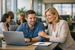 Bildet viser en mann og en kvinne som sitter foran hans PC i et kontorlandskap. Hun holder rundt hans venstre overarm. De smiler. Han har Jeans-skjorte og er mørk blond. Hun har langt blondt hår, og en beige drakt.