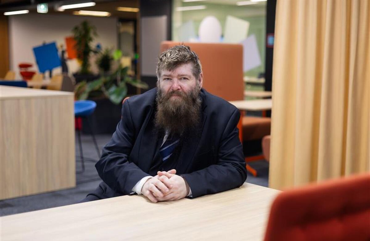 Raymond André Hagen har skjegg og dress, og sitter på et kontor. Håret er halvmørkt med grå stenk.