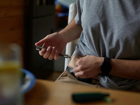 En mann setter en sprøyte på siden av sin egen kropp.