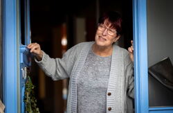 En kvinne står i en døråpning, og har blikket rettet mot en person på utsiden som vi ikke ser.