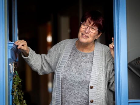 En kvinne står i en døråpning, og har blikket rettet mot en person på utsiden som vi ikke ser.