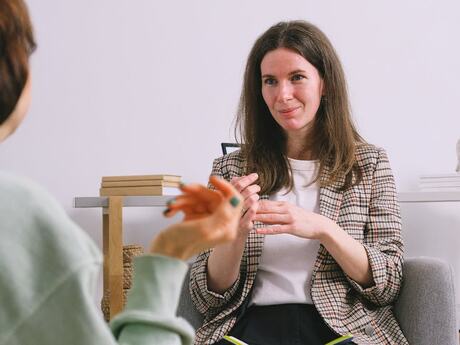 To kvinner sitter i et rom. Den nærmeste ser vi bakfra. Den andre ser empatisk ut.