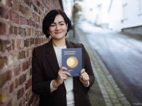 Unn Therese Omdal holder opp boka som hun har skrevet.