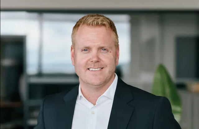 Færre telefoner, færre henvendelser og mindre dobbeltarbeid er blant klarspråkgevinstene, sier Simen Pedersen. Foto: Menon Economics Bildet er et profesjonelt portrettfoto av en mann i dressjakke og hvit skjorte som smiler mot kamera. Han er fotografert fra brystet og opp, med kort, lyst hår. Bakgrunnen er et kontormiljø som er bevisst uklart (myk bakgrunn/blur), med store vindusfla