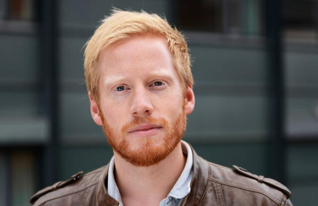 Små misforståelser i en lang henvisnings- og vurderingsprosess kan bidra til store forskjeller i hvem som får hjelp, sier Kristian Heggebø. Foto: Sonja Balci Bildet er et portrettfoto av en mann som ser rett inn i kamera med et rolig, nøytralt uttrykk. Han har kort, lyst hår og et rødlig skjegg. Han har på seg en brun skinnjakke over en lys skjorte med åpen krage. Bakgrunnen er ute eller i et urbant mil