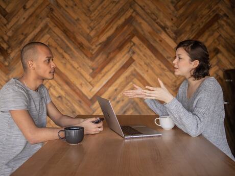 To personer i samtale ved et bord, sett fra siden, en mann og en kvinne