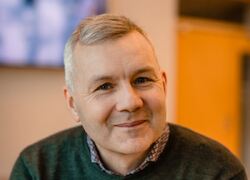 Middelaldrende mann med grått hår og genser ser inn i kameraet.