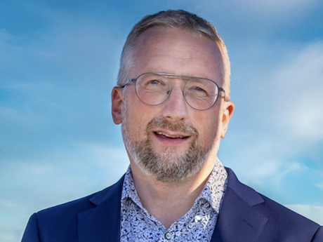 Middelaldrende mann i blå dress omgitt av blå himmel. Han smiler mot kameraet.