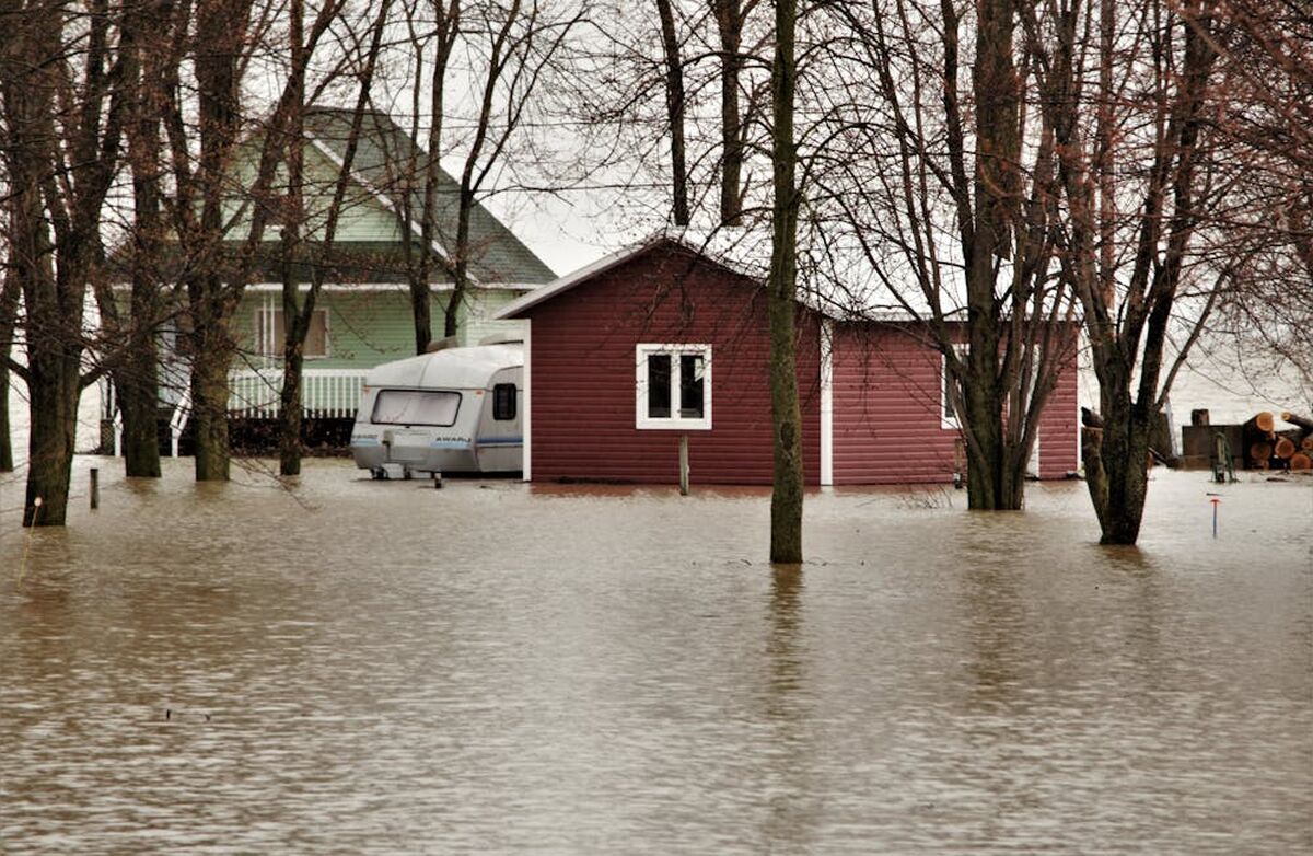 Bildet viser et område satt under vann, og vi ser et rødt uthus, et hvitt våningshus, en campingvogn.