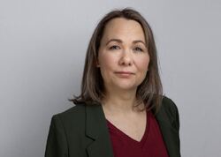 Kvinne med mørkt blondt hår, midtskill, dressjakke og burgunder V-genser ser alvorlig inn i kameraet.