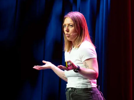 Ung kvinne med langt lyst hår holder foredrag på en scene på en konferanse