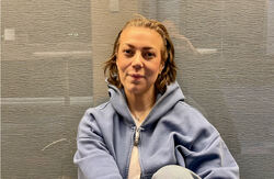 - Skal ein nå folk, må ein også gi dei noko å kjenne att, smile av eller bli litt rørte av, seier Ida Nicoline Glosimot. Foto: Torbjørn Vinje Ung kvinne sitter og ser inn i kameraet, holder hendene rundt det ene kneet. Bakgrunnen er gråsvart, og ser ut til å ha glass i front.