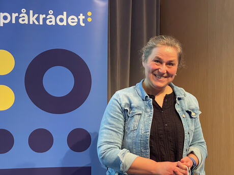 Middelaldrende kvinne med håret i hestehale ser mot fotografen. Hun har på en lyseblå jakke i dongeristoff.