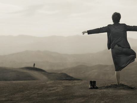 Kvinne sett bakfra i et litt dystert landskap står på ett ben