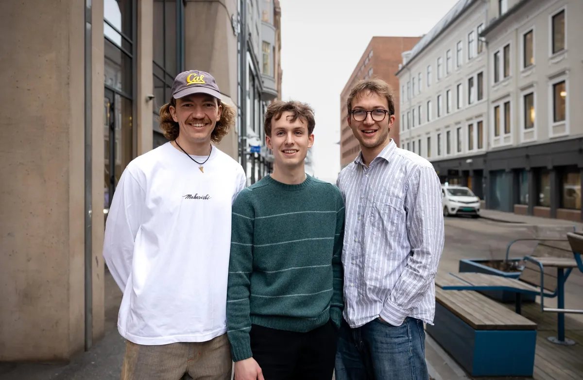 Den unge trioen vant i fjor en av Europas mest prestisjetunge KI-priser. Foto: digitalnorway.com Bildet viser tre unge menn utendørs i et bymiljø. De smiler mot fotografen, og er uformelt kledd. En av dem har cap, en har briller.