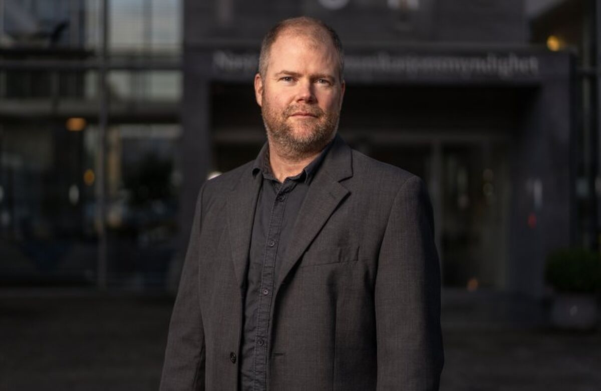 Middelaldrende mann med lite hår fotografert utendørs med en kontorbygning i bakgrunnen. Mørkt og litt dystert.