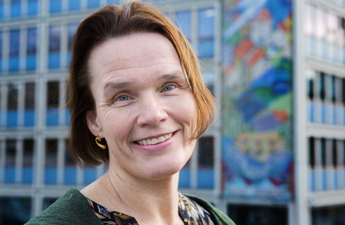 Middelaldrende kvinne smiler mot kameraet. Bildet er tatt utendørs i et bymiljø.