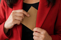 Kvinne med rød jakke stikker en brun konvolutt på innerlommen. Vi ser ikke ansiktet hennes.