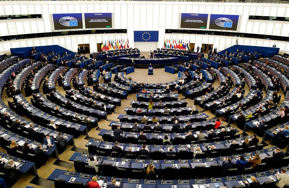 Bildet viser Europaparlamentets møtesal, som er rund. Vi ser fra høyden og ned mot scenen med diverse flagg, og medlemmene bakfra.
