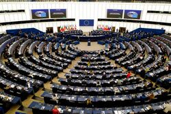 Bildet viser Europaparlamentets møtesal, som er rund. Vi ser fra høyden og ned mot scenen med diverse flagg, og medlemmene bakfra.