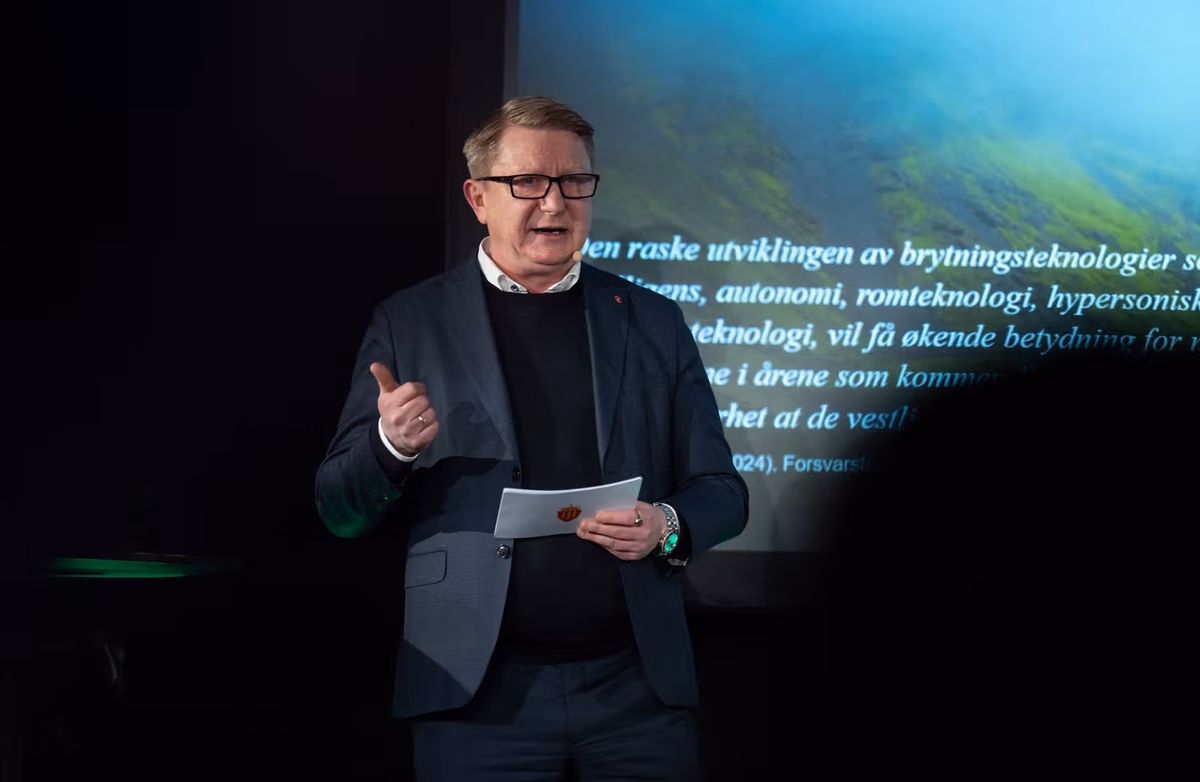 Middelaldrende mann som taler til en forsamling. Mørke klær.