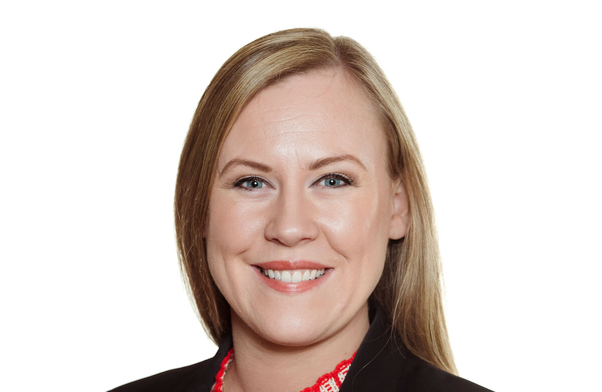 Barne- og familieminister Lene Vågslid. Foto: Astrid Waller Portrett av en smilende kvinne med lyst hår, svart jakke og rød/hvit overdel, fotografert mot lys bakgrunn. Bildet har et rent, formelt uttrykk.